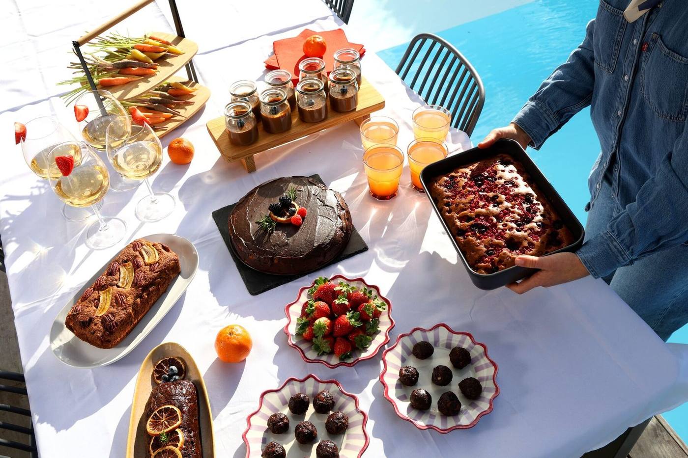 Mesa de catering ao ar livre junto à piscina com sobremesas e bebidas